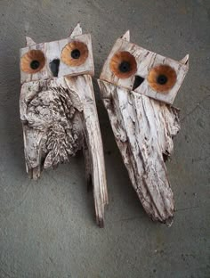 two wooden owls sitting next to each other on the ground with their eyes open and one eye closed