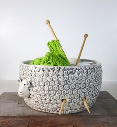 a bowl that has some knitting needles sticking out of it and a sheep head in the center