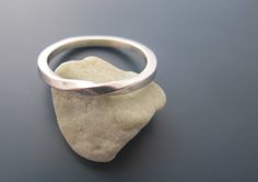 a silver ring sitting on top of a rock next to a piece of white sand