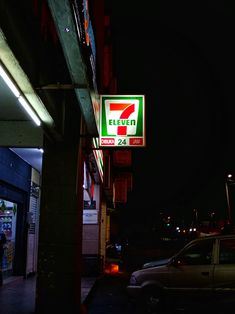 a neon 7 - eleven sign is lit up on the side of a building at night