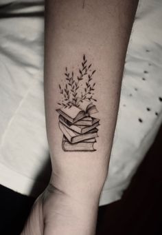 a person with a tattoo on their arm holding a stack of books and flowers in the shape of a heart