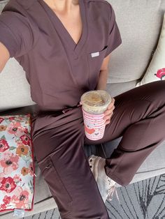 a woman in scrubs sitting on a couch holding a cup of coffee