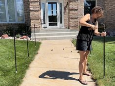 a woman standing in front of a house holding a tennis racquet on top of a sidewalk