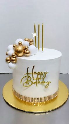 a white and gold birthday cake with candles