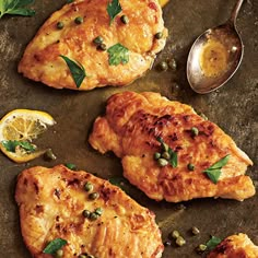 three pieces of chicken with herbs and lemons on a baking sheet next to a spoon