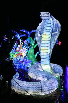 a large snake statue is lit up in the dark with lights on it's sides