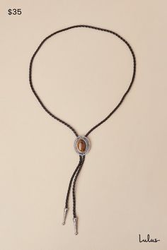 Tip your hat and up your aesthetic with the Petit Moments Western Wow Silver and Black Chunky Bolo Tie! This statement-making bolo tie has a woven faux leather cord with an adjustable, bolo-style toggle medallion at the front, which is composed of silver-toned metal and features an oversized, tiger's eye-like accent at the center. Matching embossed silver aglets complete the look. Adjustable bolo slide toggle. Necklace Measures 37" Long. 70% PU, 15% Zinc, 15% Quartz Stone. Imported. Lulus | West Bolo Tie Styling, Western Style Adjustable Bolo Ties, Bohemian Adjustable Lariat Bolo Tie, Bohemian Lariat Bolo Tie Adjustable, Bohemian Lariat Bolo Tie, Western Style Adjustable Bolo Ties For Festivals, Western Style Festival Bolo Tie, Rodeo Lariat Bolo Tie With Adjustable Length, Adjustable Brown Lariat Bolo Tie