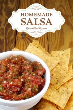 homemade salsa in a white bowl surrounded by tortilla chips on a wooden table