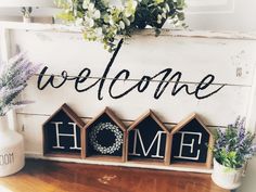 a welcome home sign on a shelf next to some flowers and potted greenery