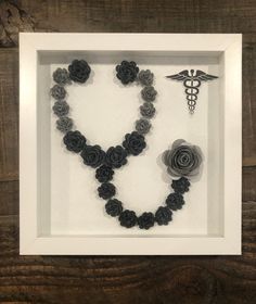 a white frame with black roses and a medical symbol on the front, hanging in a wooden wall