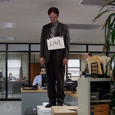 a man standing on top of boxes in an office cubicle holding a sign that says liar