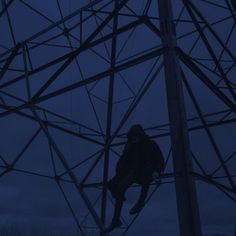 a man climbing up the side of a high voltage power line in the dark at night