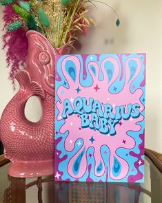 a pink and blue greeting card sitting on top of a glass table next to a vase with flowers