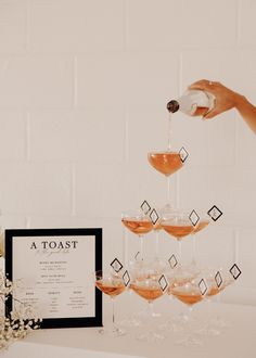 a person pouring drinks into wine glasses in front of a menu and flowers on a table