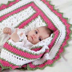 a baby wrapped up in a blanket on top of a white bedding with pink, green and white crochet