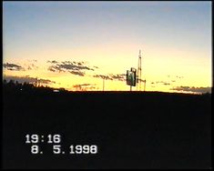 the sun is setting over a field with a clock tower in the foreground and clouds in the background