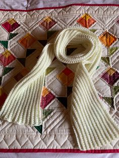 a white knitted scarf laying on top of a quilt