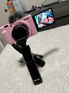 a pink camera sitting on top of a bed next to a cell phone and microphone