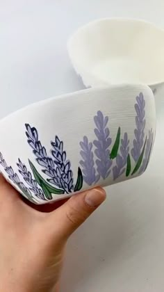 a hand holding a white bowl with purple flowers painted on it