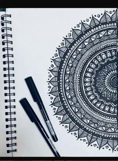 two pens are sitting next to a spiral notebook with an intricate design on the cover