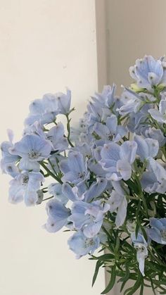 blue flowers are in a glass vase on a table next to a white wall and window