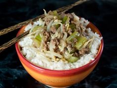 a red bowl filled with rice and meat on top of a black countertop next to two chopsticks