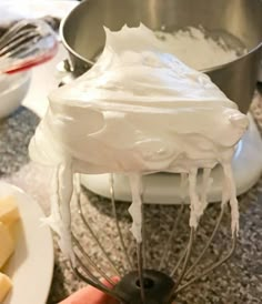 a hand holding a whisk over a bowl with cheese on the counter next to it