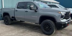 two gray trucks are parked in front of a blue building and another one is sitting next to it