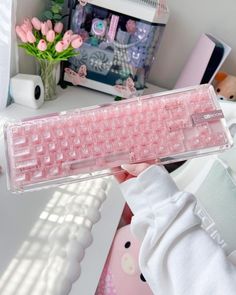 a person holding up a pink keyboard in their hand with flowers on the table behind them