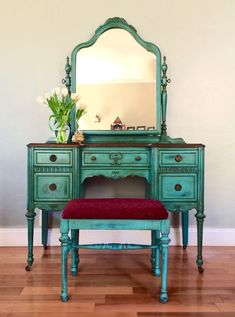 a green dresser with a mirror and red cushion on it's top sitting in front of a white wall