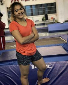 a woman standing on top of a blue trampoline in a gym with her arms crossed