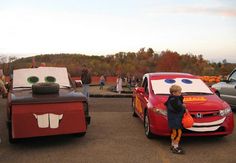 a young boy standing next to a red car in front of other cars and people