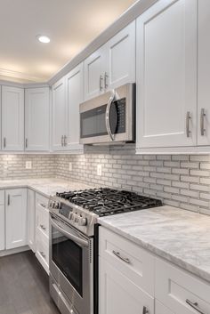 a kitchen with white cabinets and marble counter tops, stainless steel oven and stove top