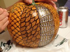 a person is carving an orange with intricate designs on it, while another hand holds the handle