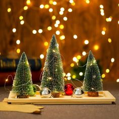 three small christmas trees sitting on top of a wooden tray next to a lit tree