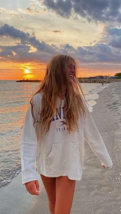 a girl walking on the beach at sunset