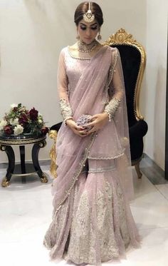 a woman in a pink lehenga standing next to a gold chair and table