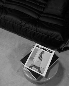 a magazine sitting on top of a glass table next to a black leather couch in a living room