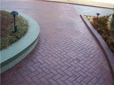 a brick walkway with two lights on each side and some bushes in the back ground