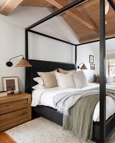 a bedroom with a four poster bed and white walls, hardwood floors, and wooden ceiling