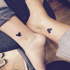 two people with matching mickey mouse tattoos on their feet, one is holding the other's hand