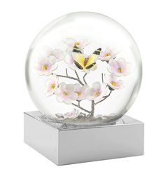 a glass ball with flowers and butterflies in it on a silver base, sitting on a white surface