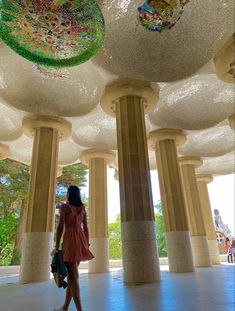 a woman is walking in the middle of a room with columns and glass balls on the ceiling