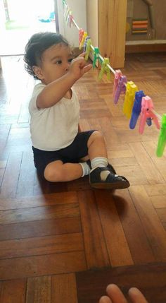 a toddler sitting on the floor playing with clothes pegs and toothbrushes