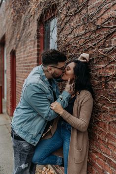 a man and woman leaning against a brick wall