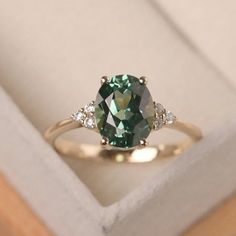 a green ring with three diamonds on it sitting in a white box next to a wooden surface