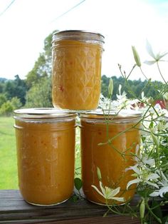 three jars filled with food sitting on top of a wooden table next to white flowers