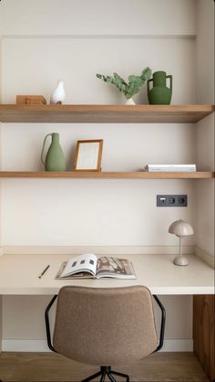 a desk with a chair, vases and books on it in front of a white wall