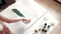 a woman is painting on the floor with her hands and paint rollers next to it