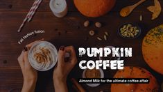 someone holding a cup of pumpkin coffee on top of a wooden table with other items around it